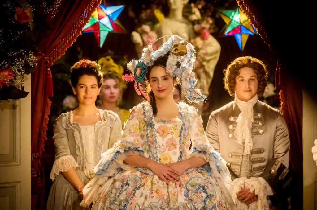 La actriz Alicia Armenteros dando vida a Luis de Orleans en uno de los capítulos de la serie de Movistar+ La vida Breve. Aparece con un traje de época, sentada junto a otros dos protagonistas.